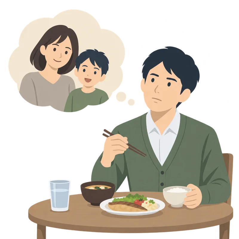 ひとりで食卓について食事をしながら、家族（妻と子ども）のことを思い浮かべる男性